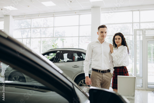 Couple buying the car. Pair in a car salon. Husband with vife choose the automobile.