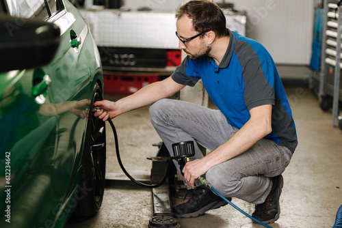 Man inflates the tires on auto service. Mechanic in glasses inspection the car at garage