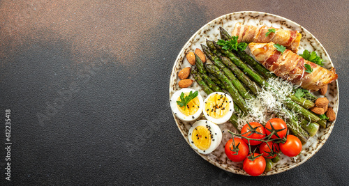 Baked chicken breast wrapped in bacon with asparagus, eggs and cherry tomato, Healthy fats, clean eating for weight loss. Keto paleo diet menu, top view photo