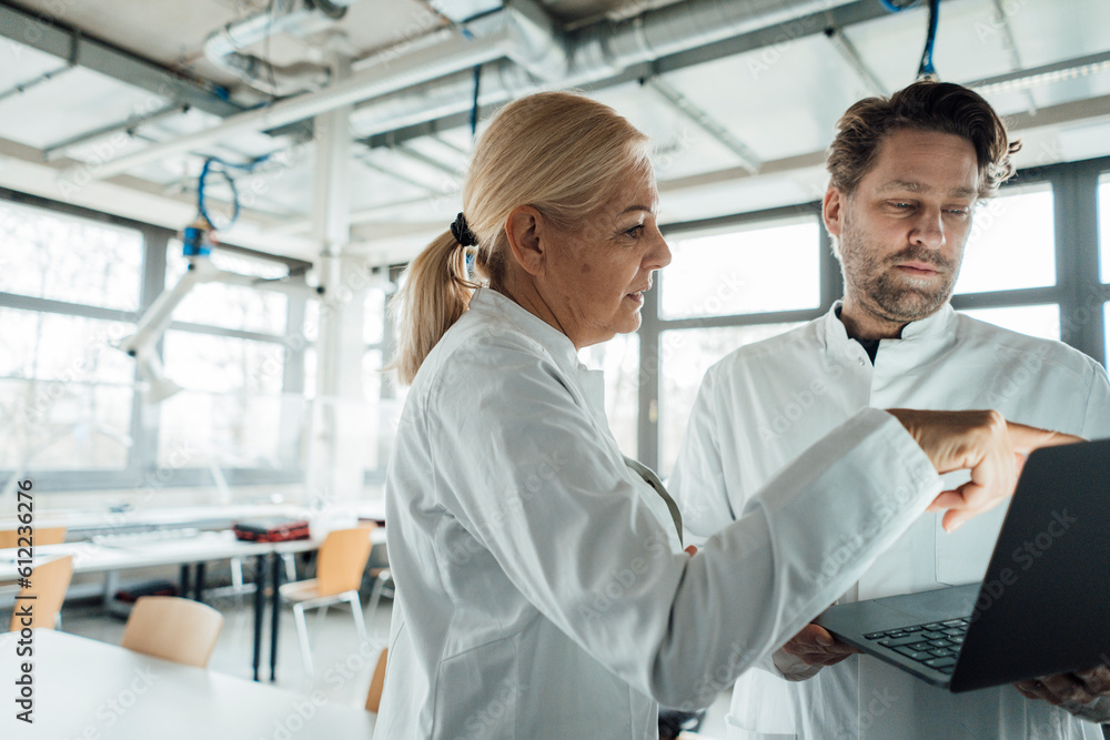 Senior scientist with colleague discussing over laptop in laboratory Senior scientist with colleague discussing over laptop in laboratory