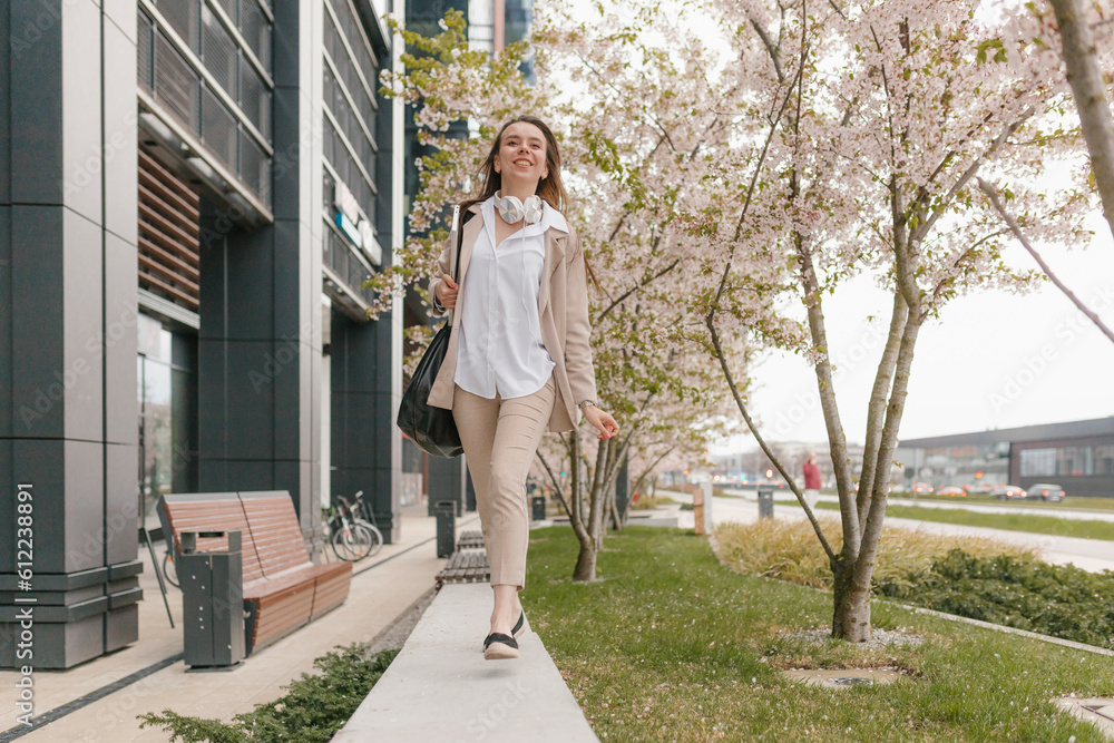 Happy young businesswoman walking in front of cherry blossom flower tree at footpath Happy young businesswoman walking in front of cherry blossom flower tree at footpath