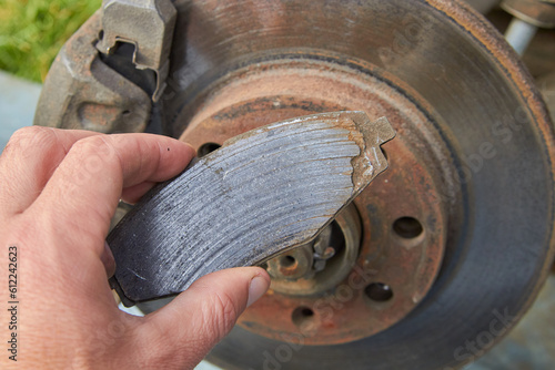 car mechanic shows a worn brake pad, a worn brake shoe and a against the background of an automobile brake disc with signs of corrosion