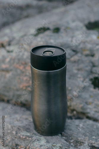 Tourist thermos mug on the background of mountains, stones and a river in which the sunset and clouds are reflected.