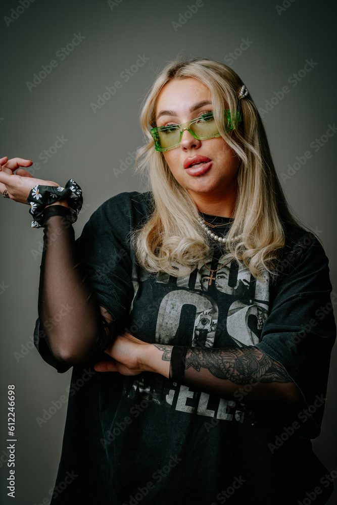 A blonde girl in green glasses and dark clothes is photographed in the studio on a dark background