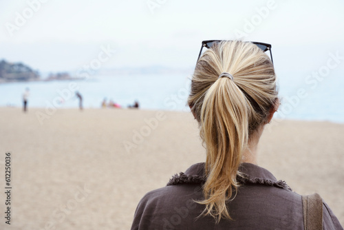 Young blonde girl with her back turned looking at the landscape with beach in the background. photo