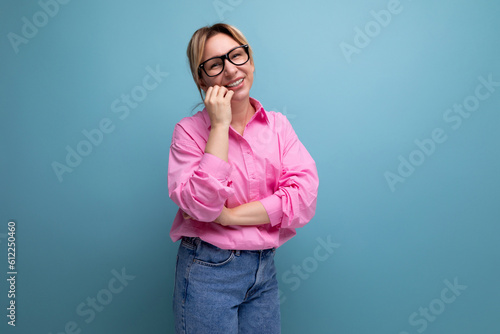 young pretty caucasian blonde secretary woman with ponytail hairstyle, glasses and in a pink shirt on a blue background with copy space