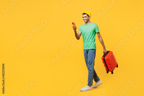 Traveler man wear casual clothes green t-shirt hat hold suitcase mobile cell phone isolated on plain yellow background. Tourist travel abroad in free time rest getaway Air flight trip journey concept #612254844