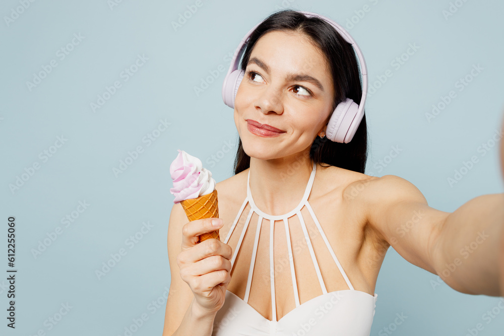 Close up young woman wear swimsuit hedphones do selfie shot pov mobile cell phone eat ice-cream look aside near hotel pool isolated on plain blue background. Summer vacation sea rest sun tan concept. Close up young woman wear swimsuit hedphones do selfie shot pov mobile cell phone eat ice-cream look aside near hotel pool isolated on plain blue background. Summer vacation sea rest sun tan concept.