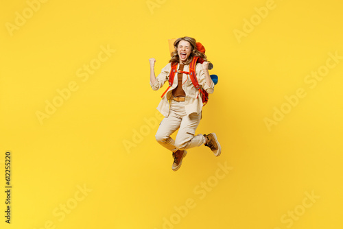 Full body young woman carry bag with stuff mat jump high do winner gesture isolated on plain yellow background. Tourist leads active lifestyle walk on spare time. Hiking trek rest travel trip concept.