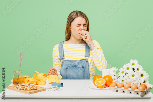 Sick unhealthy ill allergic woman has red watery eyes runny stuffy sore nose suffer from allergy trigger symptoms hay fever sit near food spread hand cough isolated on plain green background studio. photo