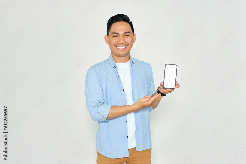 Happy young Asian man in casual clothes pointing index finger at mobile phone with blank screen isolated on white background. Advertising new mobile app, mockup concept Happy young Asian man in casual clothes pointing index finger at mobile phone with blank screen isolated on white background. Advertising new mobile app, mockup concept