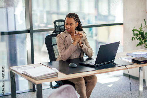 African American female company finance manager executive using a laptop sitting at the desk.