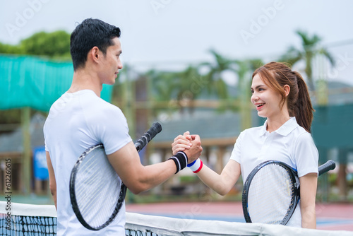 Shot of two happy tennis players players shaking hands over the net after after a competitive match.