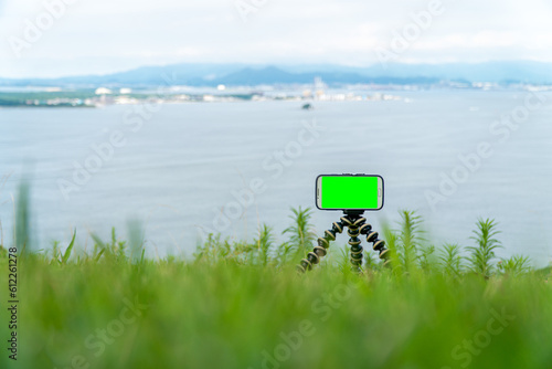 Smartphone on a tripod with green screen on it. Mobile smartphone with a chroma key green screen in the natural background.