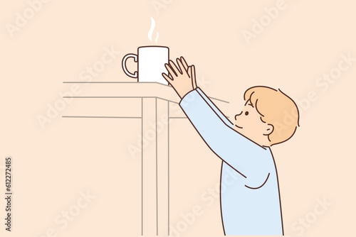 Boy reaches for mug of hot tea on table at risk of getting burned and getting into trouble