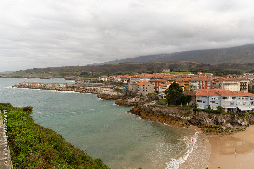 Stunning panoramic and aerial view of the Sablón beach in the town of Llanes with tourists and people strolling along its golden sand and calm love during a cloudy day in asturias.