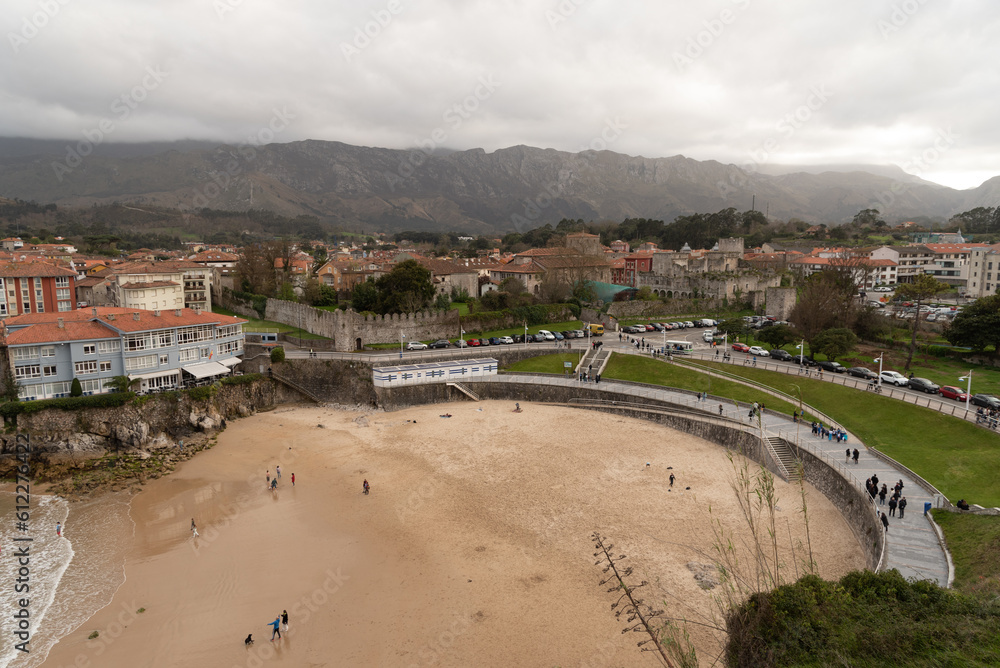 Impressive panoramic and aerial view of the Sablón beach in the town of Llanes with tourists and people strolling along the golden sand on a cloudy day in Asturias.