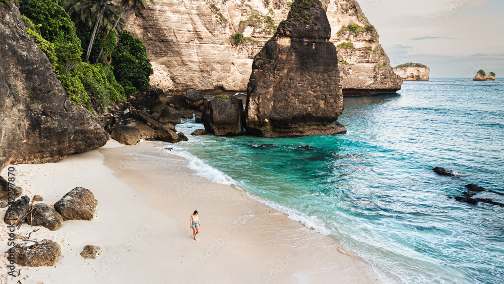 Podróżnik idący po pięknej plaży Diamond, na Indonezyjskiej wyspie Nusa Penida, plaża, skały klif oraz ocean. - obrazy, fototapety, plakaty 