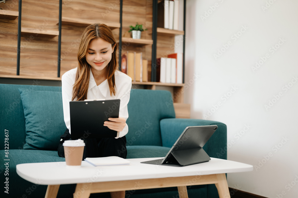 Young beautiful woman using laptop and tablet while sitting at her working place. Concentrated at work. in living room on the sofa at home office. Young beautiful woman using laptop and tablet while sitting at her working place. Concentrated at work. in living room on the sofa at home office.