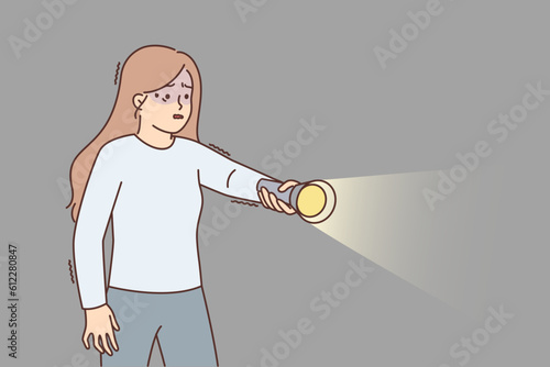 Frightened girl with flashlight walks in dark suffering from nyctophobia and trembling with fear