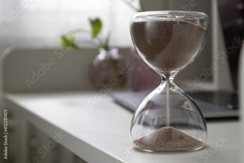 Hourglass on a white table against the background of an open laptop close-up