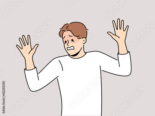 Frightened man raises hands in surrender and demonstrates obedience and refusal to resist. Frightened guy experiencing panic attack due to phobia associated with psychological trauma