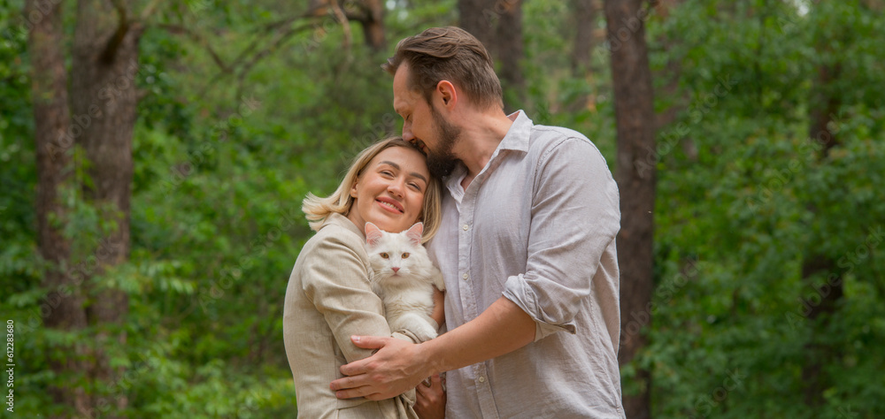 happy couple walks resting in the forest park with a white cat.portrait of a happy couple with a pet on the background of the park forest during a vacation happy couple walks resting in the forest park with a white cat.portrait of a happy couple with a pet on the background of the park forest during a vacation