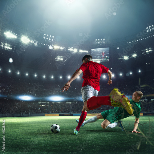 Live match. Football players in uniform during game  playing at 3D stadium with flashlights and blurred audience on background. Concept of professional sport  championship  game  achievement