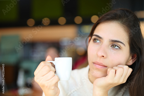 Pensive serious woman holding coffee in a bar