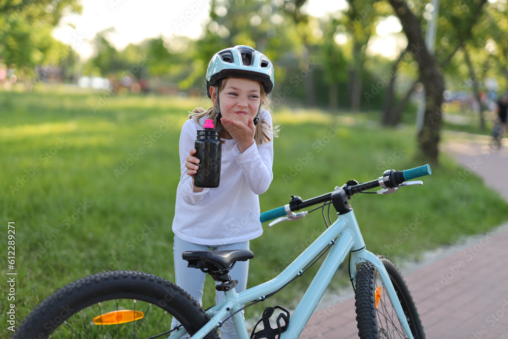 Girl child drinks water from a bottle in the park, rides a bike. Girl child drinks water from a bottle in the park, rides a bike.