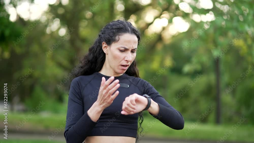Disappointed young sportswoman checking the results of training by looking at smart watch in urban city park Sad female is dissatisfied with the negative workout indicators seen on the fitness tracker Disappointed young sportswoman checking the results of training by looking at smart watch in urban city park Sad female is dissatisfied with the negative workout indicators seen on the fitness tracker