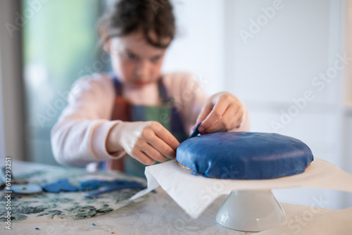 young caucasian girl child cooking baking blue icing fondant decorate cake kitchen stand party birthday