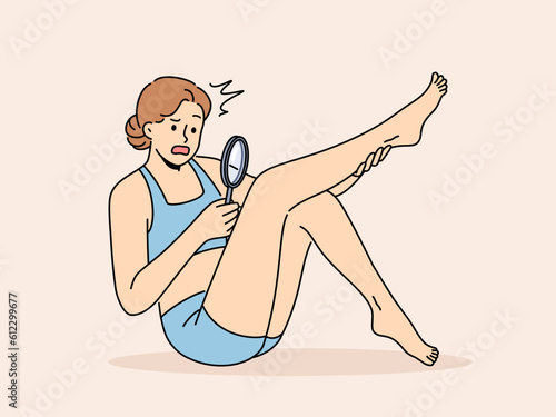 Woman is shocked by hair on legs and needs depilation or epilation in spa salon. Girl holding magnifying glass examining hair on legs for advertisement epilation services or body dysmorphic concept photo