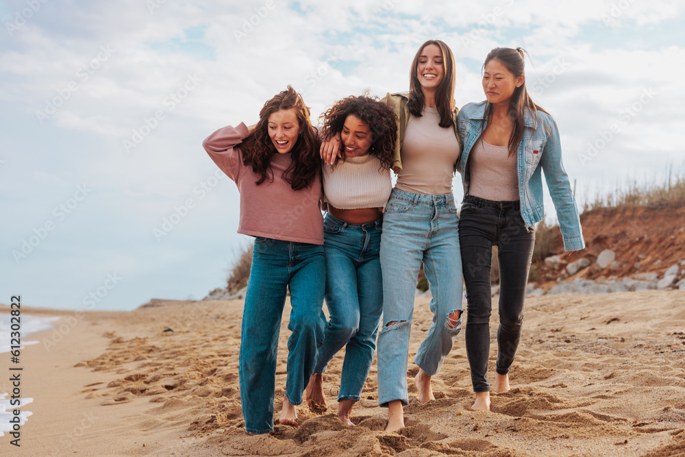 Friendship group of four diverse young women walking together on beach Friendship group of four diverse young women walking together on beach