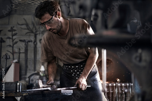 Blacksmith hammering iron at anvil in forge