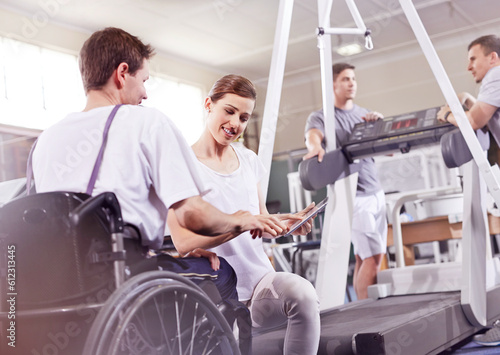 Physical therapist showing digital tablet to man in wheelchair