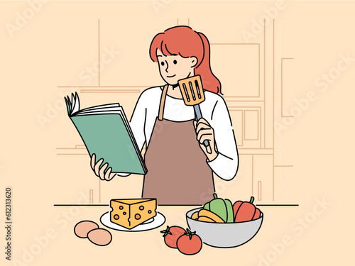 Woman with cookbook is standing in kitchen wanting to cook delicious dinner and vegetables and cheese with eggs. Girl cook in apron uses cookbook while preparing salad or appetizers