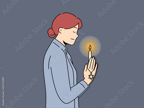 Praying jewish woman with star of david and burning candle in hand for international holocaust remembrance day concept. Jewish praying girl turns to god standing in synagogue and reading prayers