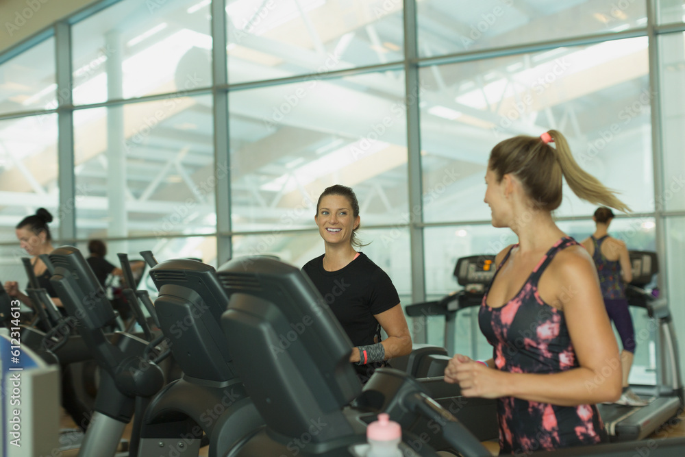Smiling women talking and jogging on treadmills at gym Smiling women talking and jogging on treadmills at gym