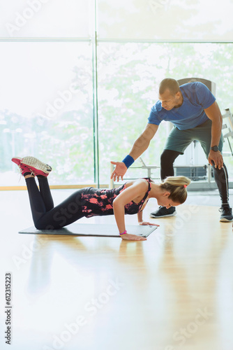 Fototapeta Naklejka Na Ścianę i Meble -  Personal trainer guiding woman doing push-ups on knees at gym