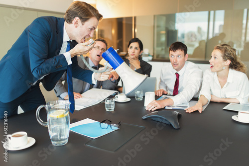 Shocked colleagues watching businessman megaphone yelling into conference phone photo