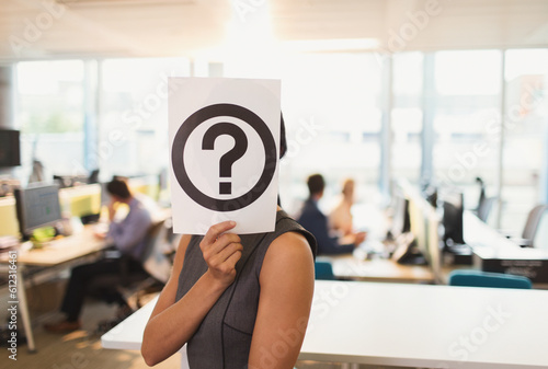 Фотография Portrait businesswoman holding question mark printout over her face in office