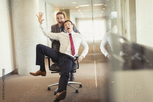 Canvas Print Playful businessman pushing colleague down corridor in office chair