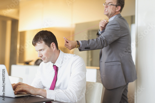 Photos Angry businessman aiming rubber bat unsuspecting businessman working at laptop