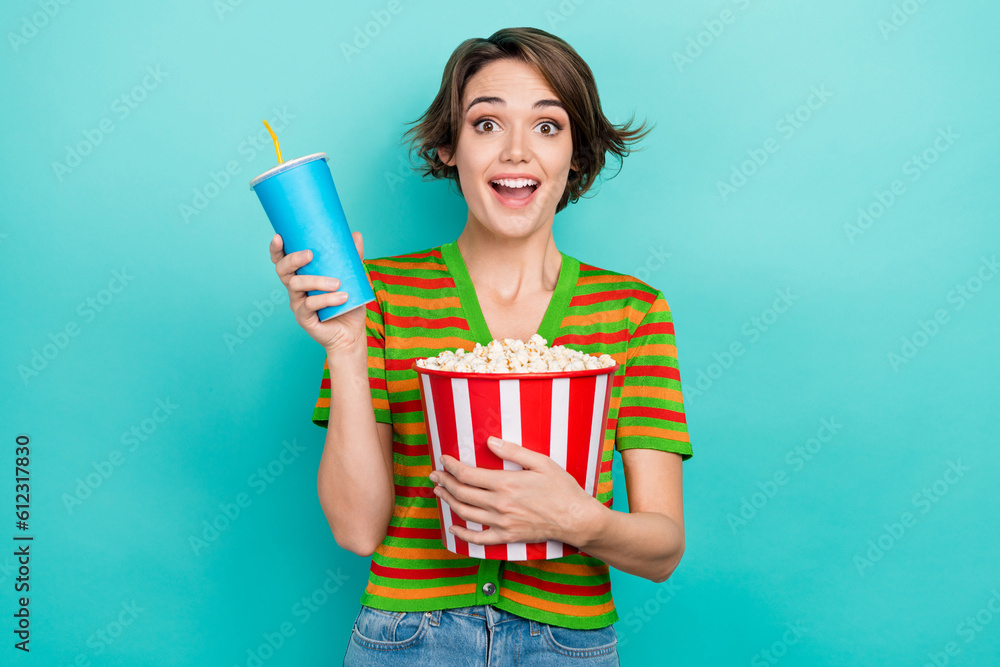 Photo of excited funky woman dressed striped t-shirt holding pop corn bucket soda cup isolated turquoise color background Photo of excited funky woman dressed striped t-shirt holding pop corn bucket soda cup isolated turquoise color background