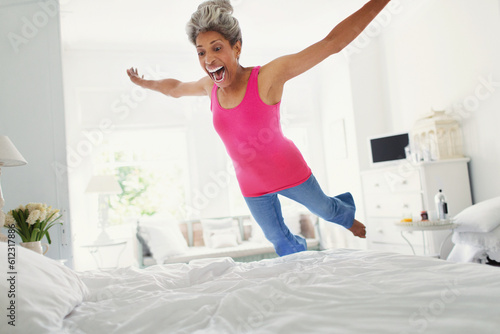 Playful mature woman jumping onto bed