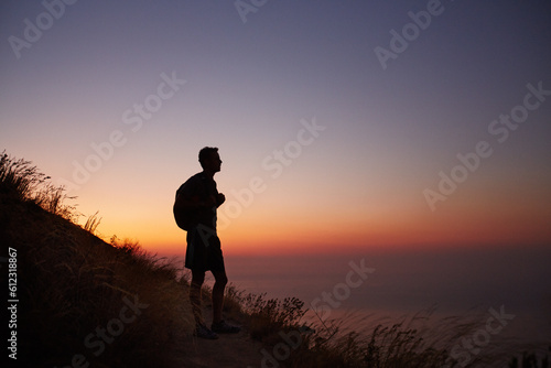 Silhouette of male hiker on trail overlooking ocean at sunset