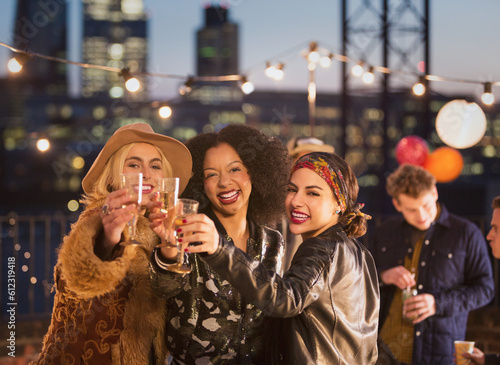 Portrait enthusiastic young adult friends toasting champagne flutes at nighttime rooftop party