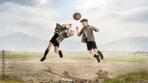 Head kick. Active little boys, children, friends in retro style clothes playing football outdoors on a daytime. Warm sunny day