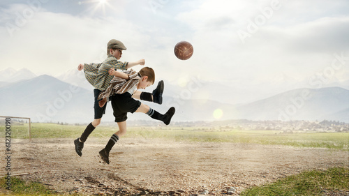 Playful little boys, children in retro style clothes playing football, kicking ball in jump outdoors on a daytime
